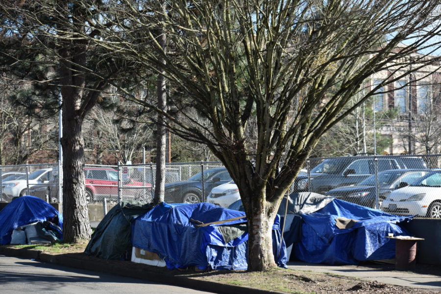 A cluster of tents sits on and near the sidewalk next to the Cleveland staff parking lot on Franklin Street. More tents extend around the corner behind the parking lot on 25th Avenue just behind the lot.