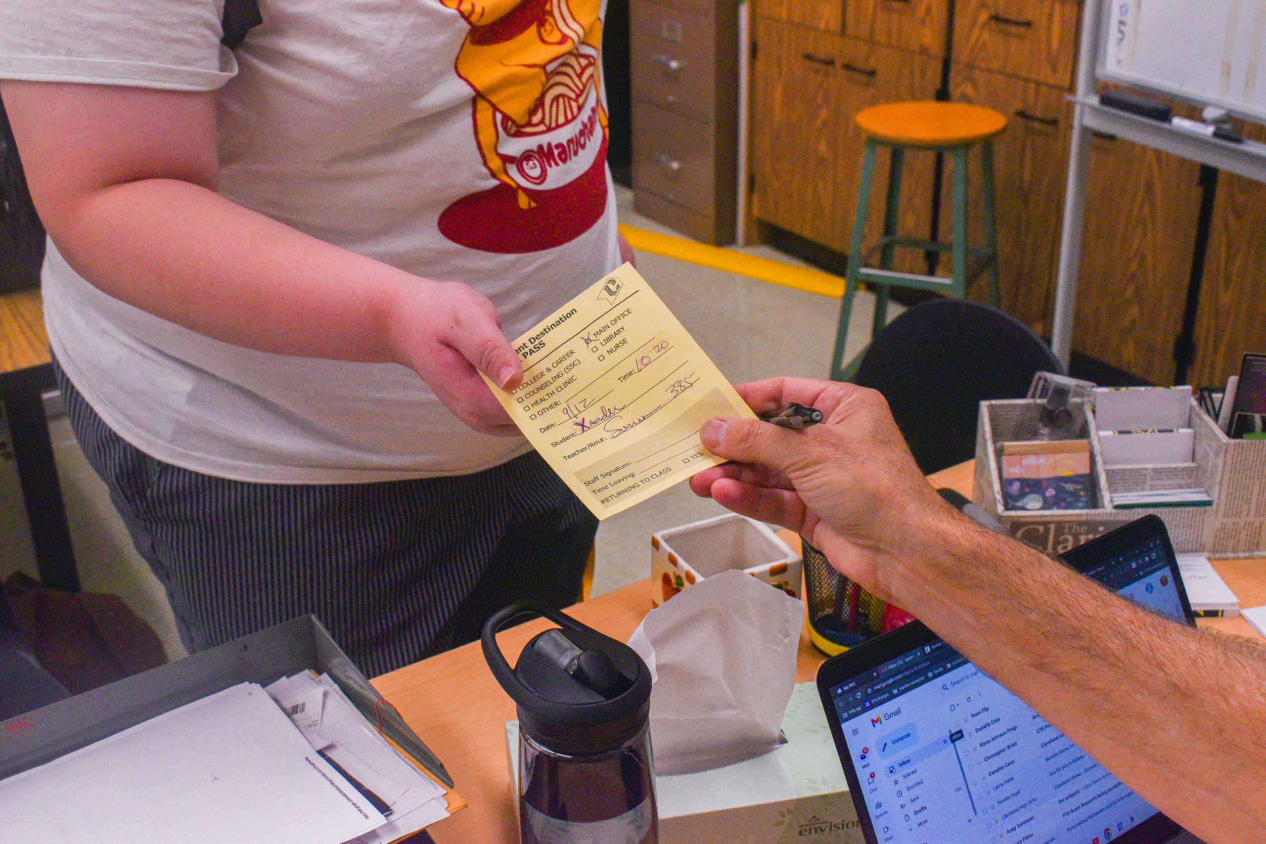 Journalism teacher Andy Sorensen hands out a student destination hall pass  to a student.